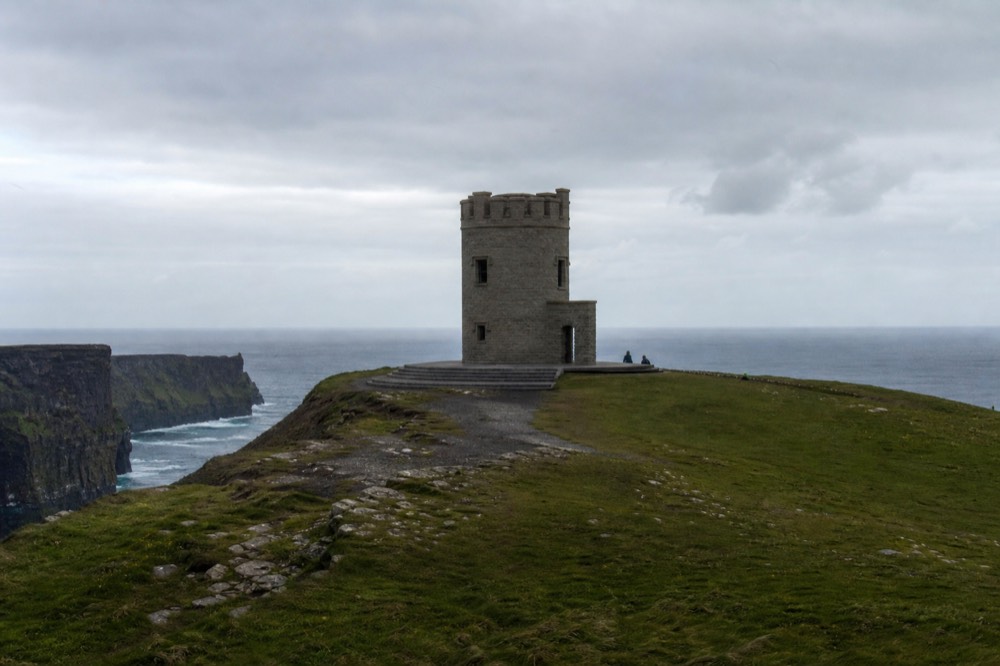 The stone watchtower of Moher Tower standing on the wild southern headland of Hag's Head, sheer cliffs dropping to the Atlantic on either side under a broad sky.