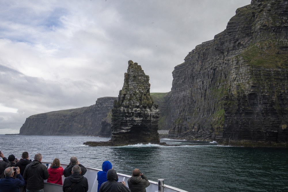 The An Branan Mor sea stack rising sheer from the ocean at the foot of the Cliffs of Moher, its ledges pale with nesting seabirds, the cliff wall behind.