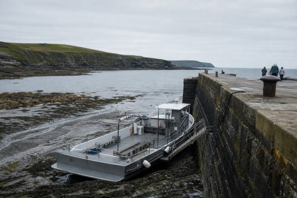 The stone quay at Doolin Pier at low water, a tour boat sitting well below the harbour wall with a gangway step down to its moving deck.